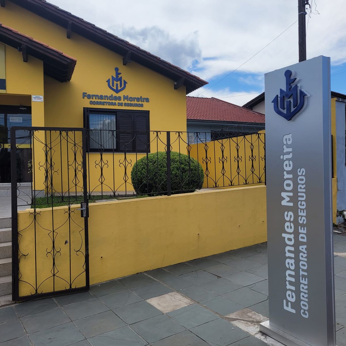 Fachada da Fernandes Moreira Corretora de Seguros, com a logo na parede e o totem na calçada